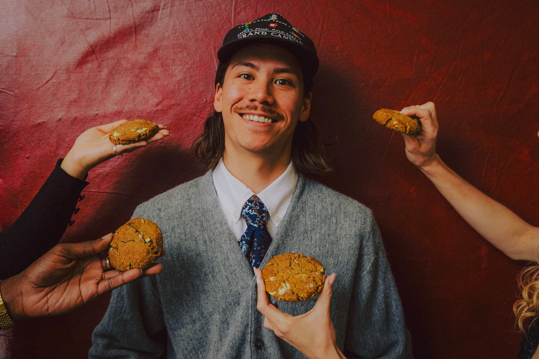 A man smiling as four hands offer him cookies